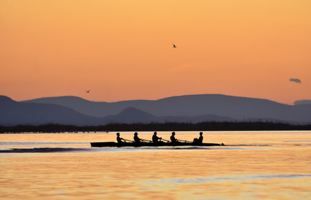 Silhouette of people rowing on a boat at sunsetの写真素材