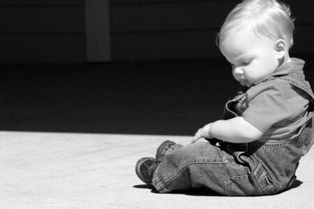 Caucasian toddler sitting pensively on the groundの写真素材