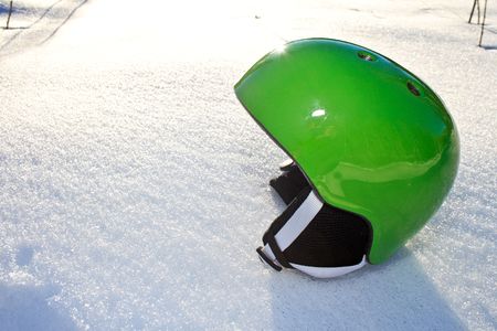Bright green snowboarding helmet sitting on the snow on a sunny dayの写真素材