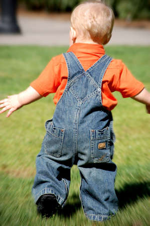 Caucasian male toddler in denim running in a grassy park