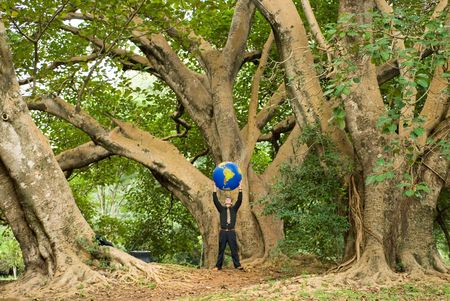 Wide angle shot of a Latin American businessman standing in a grove of trees with an inflatable globe held above his headの写真素材
