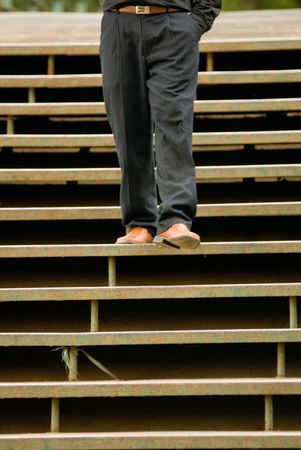 A businessman, shot from the waist down, taking step down a flight of stairs.