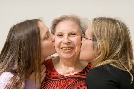 Mother and daughter on either side of their grandmother planting a kiss on her cheek. Isolatedの写真素材
