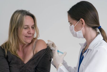 Older female patient getting an injection from a younger female doctor. Isolated.の写真素材