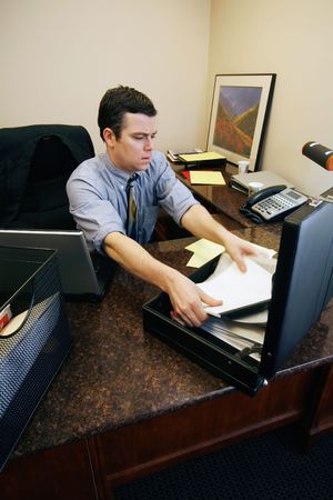 Businessman with his sleeves rolled up sitting at his desk in his office surrounded by work and...
