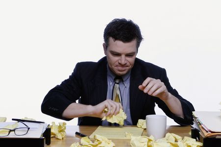 Businessman sitting at his desk looking dejected surrounded by scraps of yellow notepaperの写真素材