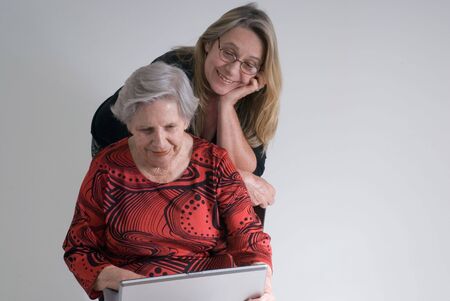 A shot of an adult child watching her elderly mother successfully using a computer.