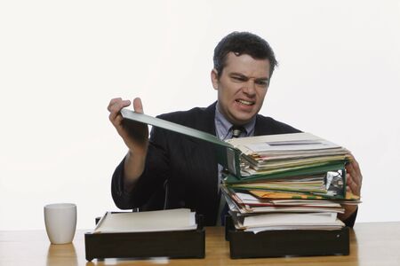 Man in a business suit sitting at his desk, staring at a large pile of folders in his inbox. Isolated against a white backgroundの写真素材