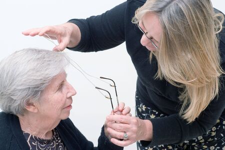 Adult woman helping an elderly lady with her reading glasses. Isolated.の写真素材