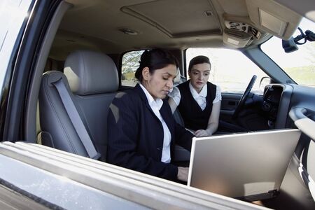 Two female colleagues working on a laptop while sitting outside in their carの写真素材