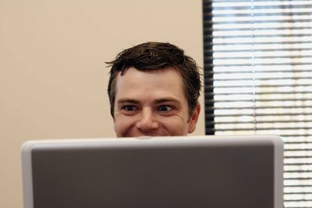 Businessman sitting behind a laptop smiling as he reads the screen. Horizontally framed shot.の写真素材