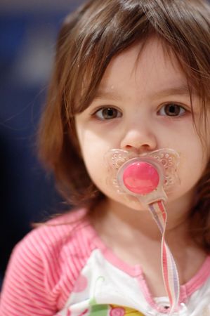 Cute young girl with a pacifier in her mouth. Vertically framed close-cropped shot.