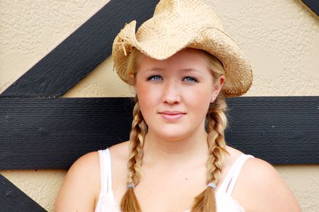 Horizontally framed outdoor shot of a smiling teenage girl, with blond hair and blue eyes, standing next to barn door wearing a straw cowboy hat.の写真素材