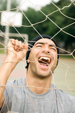 A man holding onto a soccer goal net, smiling and yelling though it. - vertically framedの写真素材