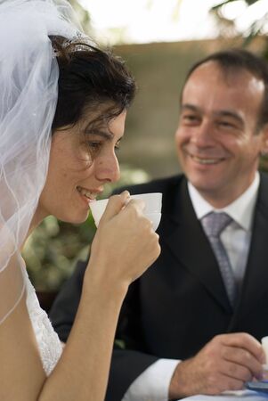 A newly married wife drinking from a teacup, her husband stares at her. - vertically framedの写真素材