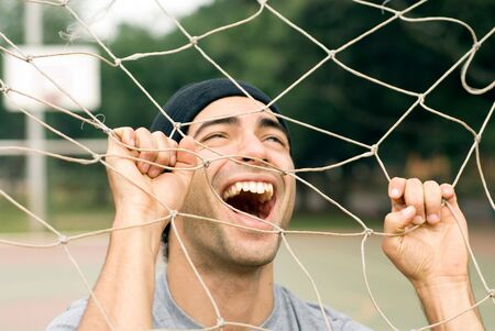 A man playing with a soccer goal net, screaming and laughing through it, while holding onto it. - horizontally framedの写真素材