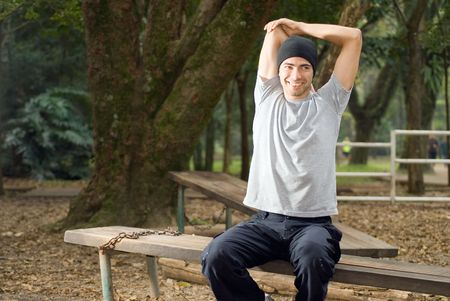 A male, sitting on a park bench, stretches his arms while smiling - horizontally framedの写真素材
