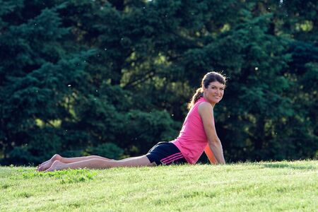A woman, lying in the grass, stretches her back, smiling - horizontally framed