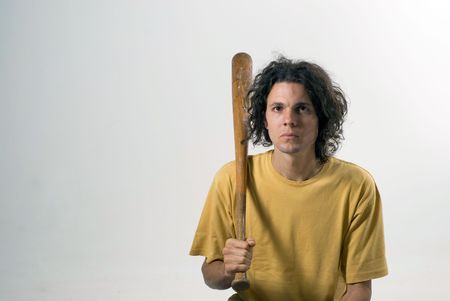 A man holding a  baseball bat and sitting on the floor with a serious look on his face. Horizontally...