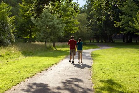 Rear view of a couple holding hands and walking down a path in green park. Horizontally framed shot.