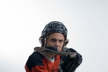 A man stands looking serious, wearing a hockey uniform. He holds out his hockey stick, balancing a puck. Horizontally framed shot.の写真素材