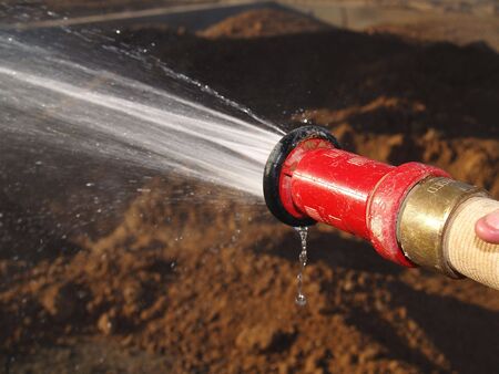 A man is holding a hose and spraying the ground at an excavation site.  Horizontally framed shot.の写真素材