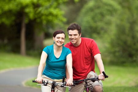 A more closer shot of a young couple, hugging and smiling at the camera and sitting on their bicycles.- horizontally framedの写真素材