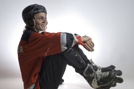 Seated hockey player smiles. He is wearing roller blades and hockey gear. Horizontally framed photographの写真素材