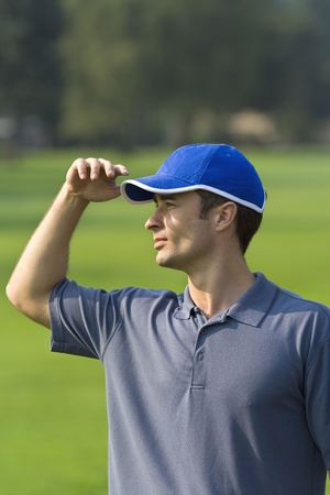 Man's profile while standing on golf course shielding eyes from sun - Vertically framed photoの写真素材