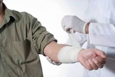 A patient is sitting in a wheelchair at a doctors office.  The doctor is bandaging his arm.  Horizontally framed shot.の写真素材