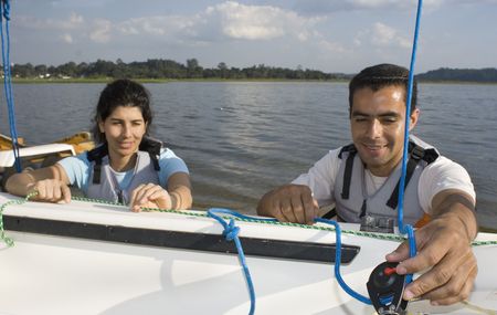 Man and woman smiling while rigging sails on sailboat. Horizontally framed photo