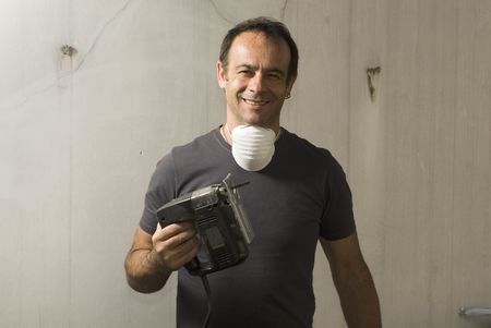 A man, holds a saw in one hand while smiling and wearing a mask on his neck. Vertically framed shot.の写真素材