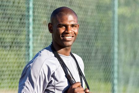 A young, attractive man is standing on a tennis court.  He is holding a jump rope around his neck and smiling at the camera.  Horizontally framed shot.の写真素材