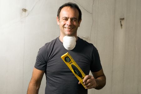 A man is standing in an unfinished apartment.  He is holding a spirit level and smiling at the...