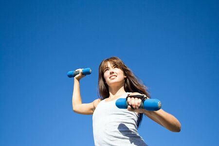 An attractive, fit woman is doing cardio with hand weights.  She is smiling and looking away from the camera.  Horizontally framed shot.の写真素材