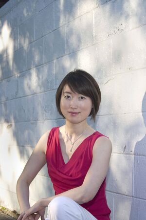 Woman kneeling beside white wall. She is smiling at camera. Vertically framed photo.