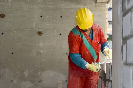The worker is busy grouting the gaps between the cinder blocks.  Concrete wall looms behind and he...