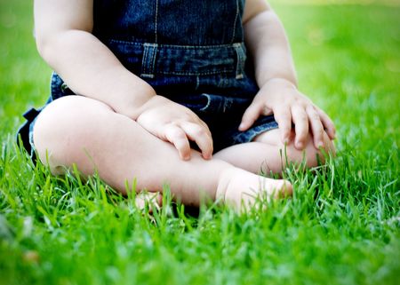 Toddler sitting on grass with jean overalls on. Horizontally framed shot.の写真素材