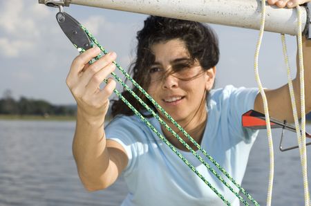 A young woman is fixing the sail on her boat.  She is looking away from the camera. Horizontally...