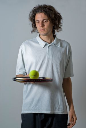 Male athlete holding a tennis racket and balancing a ball on it.  He is looking at the tennis ball.  Vertically framed shot.の写真素材