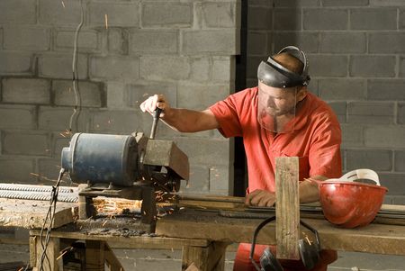 Construction worker cuts rebar with chopsaw. Horizontally framed photo.
