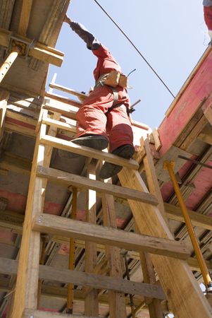 Construction worker stands on ladder. Photo taken from below. Vertically framed photo.