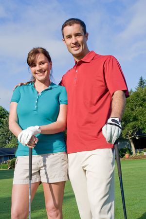 Golfers stand in front of camera. Man has arm around woman and they are smiling at camera. Vertically framed photo.の写真素材