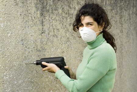 Woman wearing a paint mask holding a drill. Horizontally framed photo.の写真素材
