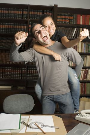 Woman rides on man's back. They are playing in the library. Vertically framed photo.の写真素材