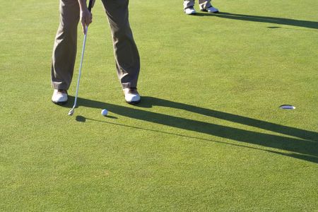 A man is standing on the green of a golf course.  He is about to putt the ball into the hole.  Horizontally framed shot.の写真素材