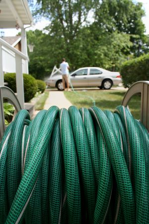 Close-up view of a garden hose.  There is a man using it to wash his car in the distance.  Vertically framed shot.の写真素材
