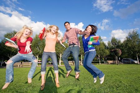 Four teen students carrying books, jumping and laughing outside. There is one boy and three girls....