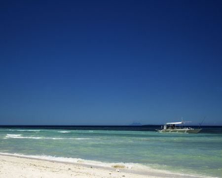 This is a tropical resort, the perfect vacation spot.  There's a boat, blue skies and water.  The names on the boat have been removed and the figures are not identifiable.の写真素材