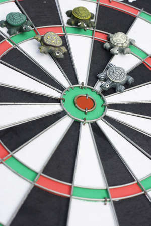 Some models of turtles are heading towards the center of a dart board.  This is a concept on slow progress towards a goal.  This could be presented as a problemの写真素材